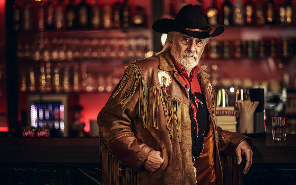 Älterer Mann mit Cowboyhut und Fransenjacke an einer Bar