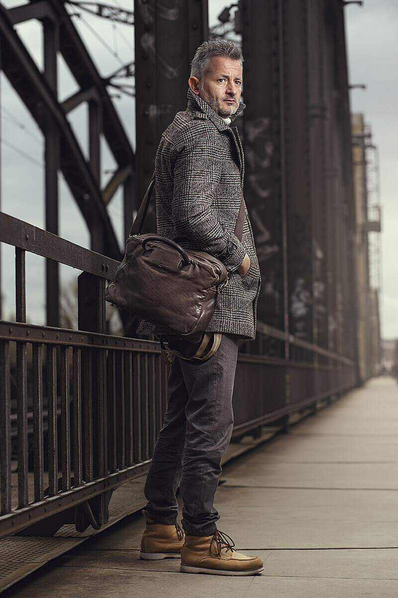 Mann mit Ledertasche auf einer Stahlbrücke