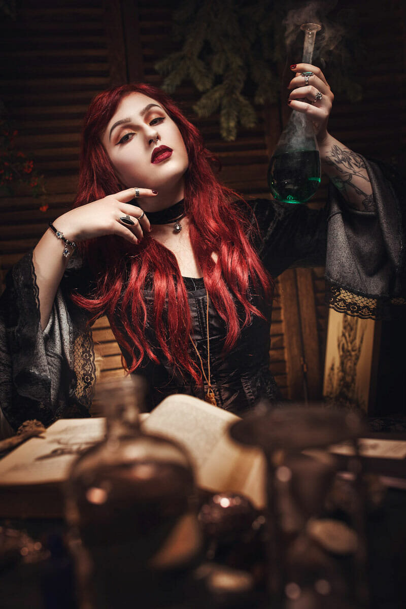 Frau mit roten Haaren in Fantasy-Inszenierung mit Buch und Flasche